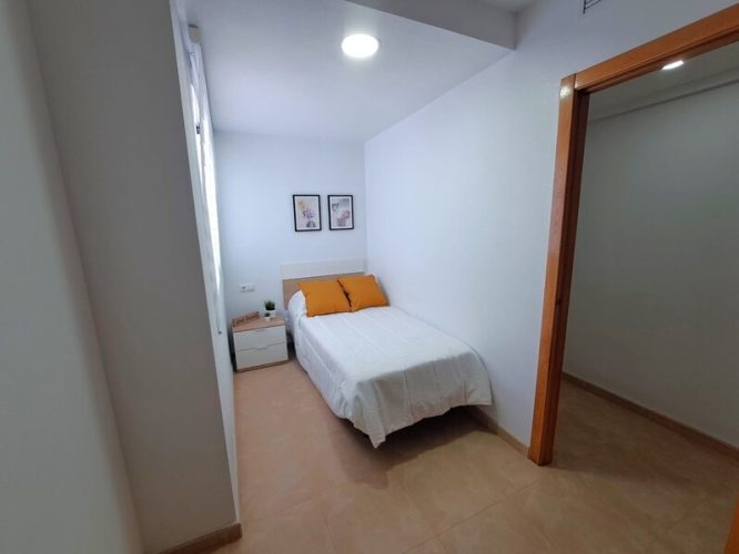 Primer plano del dormitorio de invitados con cuadros, mesilla de noche y ventana