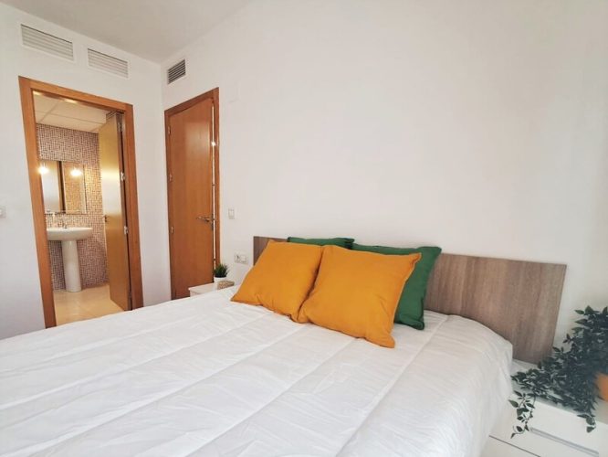 Primer plano de un dormitorio conectado al salón y a un baño, con dos mesillas de noche