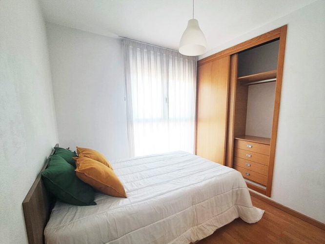 Segundo plano de un formitorio con armario que cuenta con cajonera, ventana y dos mesillas de noche