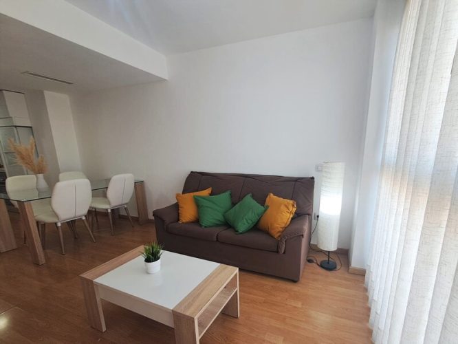 Primer plano de un salon que cuenta con sofá, mesilla, mesa de comedor, sillas y un ventanal