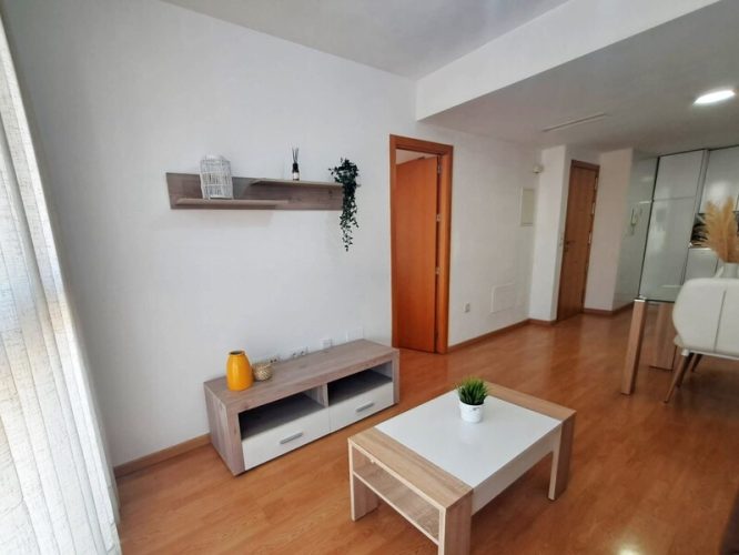 Primer plano de un salon que cuenta con sofá, mesilla, mesa de comedor, sillas, un ventanal y un estante