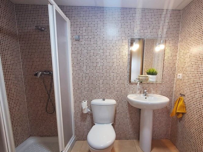 Un cuarto de baño que cuenta con ducha con mámpara, retrete, lavabo y espejo