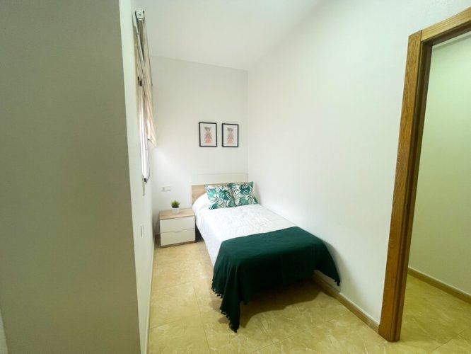 Dormitorio de invitados con una cama individual, una ventana que da al patio interior y una mesita de noche