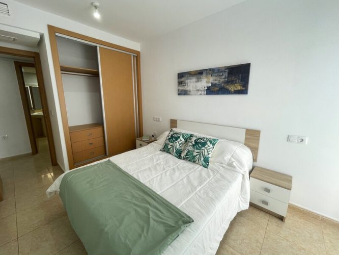 Dormitorio principal con una cama de matrimonio, dos mesitas de noche y un armario empotrado con cajonera