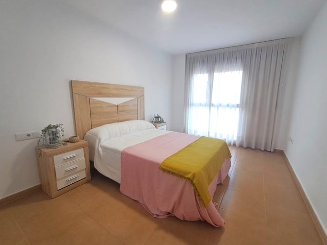 Primer plano del dormitorio principal con cama de matrimonio, dos mesitas de noche y un ventanal con cortinas