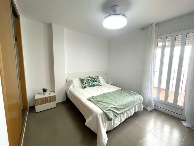 Dormitorio principal con una cama de matrimonio, dos mesitas de noche y un ventanal que da a la terraza