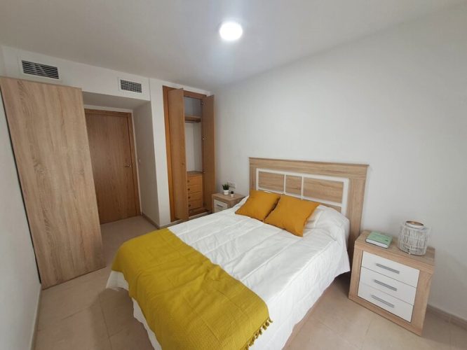 Primer plano del dormitorio con un ventanal, dos armarios, uno con cajonera y dos mesitas de noche