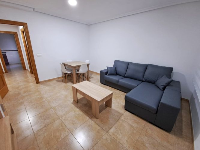 Primer plano del salón con una mesa y tres sillas, una mesita pequeña y un sofá en forma de L